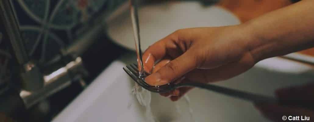 Une main qui nettoie une fourchette, tout faisant couler l'eau de l'évier