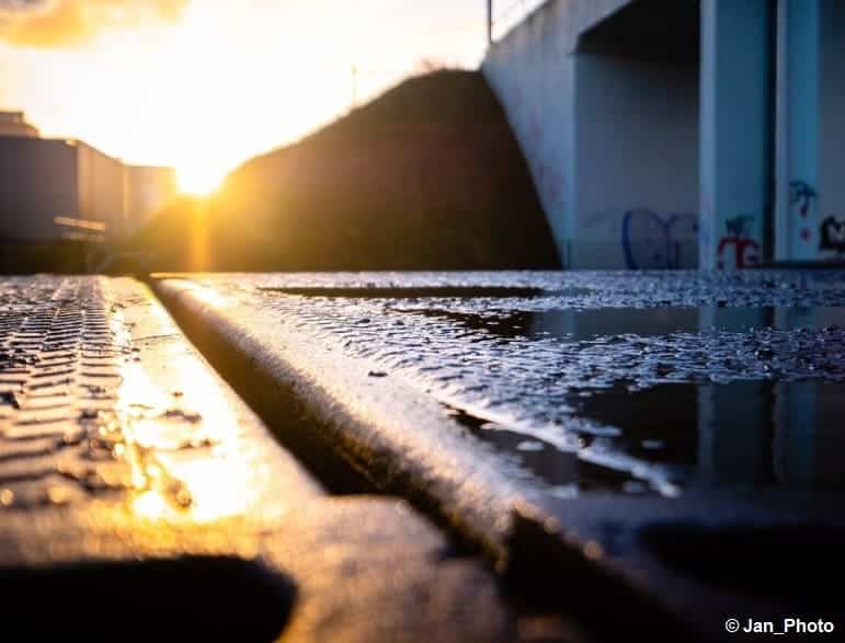 Soleil levant qui éclaire un sol bétonné, présentant des flaques d'eau