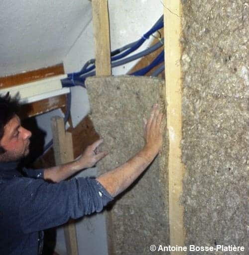 Un ouvrier qui pose sur un mur un isolant en chanvre en rouleaux.