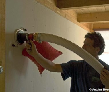 Un maçon qui isole un mur, à l'aide d'une machine qui insuffle de la ouate de cellulose