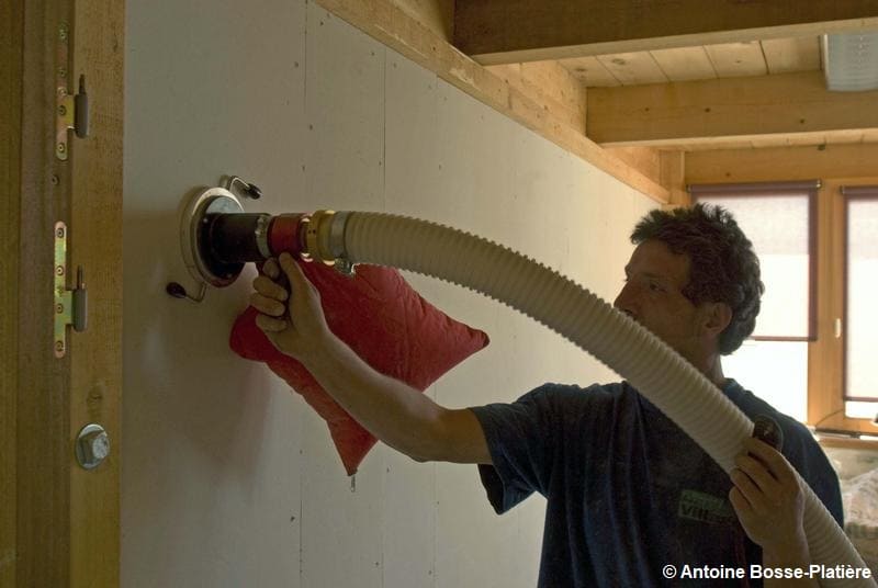 Un maçon qui isole un mur, à l'aide d'une machine qui insuffle de la ouate de cellulose