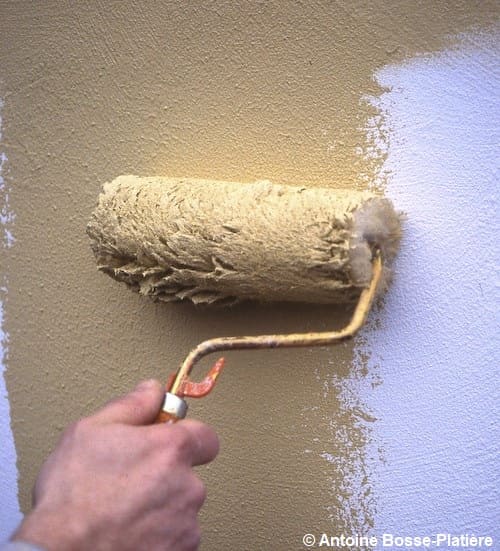 Application au rouleau d'une peinture marron claire sur un mur