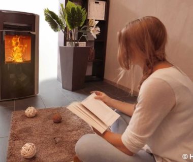 Une jeune femme assise par terre, entrain de lire un livre, devant un poêle à granulés en fonctionnement