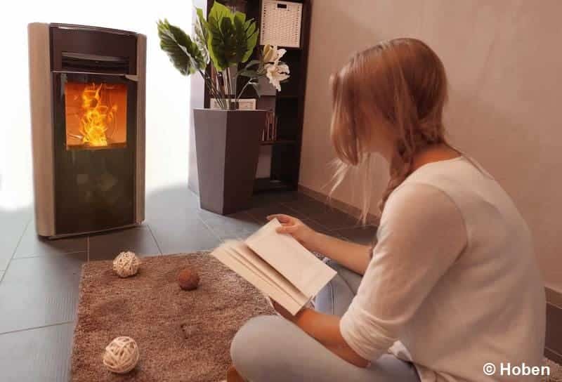 Une jeune femme assise par terre, entrain de lire un livre, devant un poêle à granulés en fonctionnement