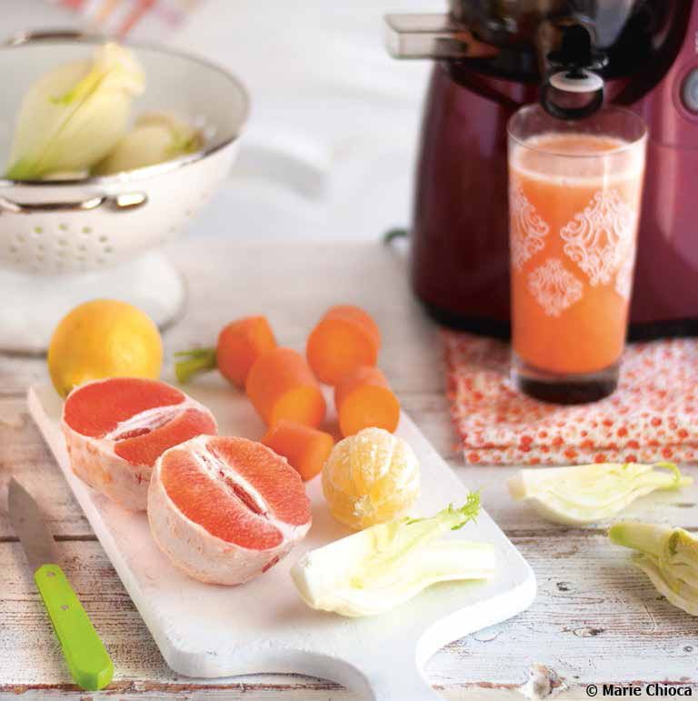 Carotte, pomelo, fenouil et citron sur une planche de travail à côté d'un verre rempli de jus