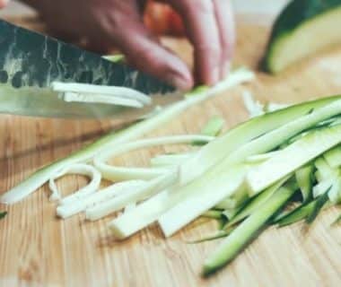 Courgette entrain d'être coupée au couteau en lamelles