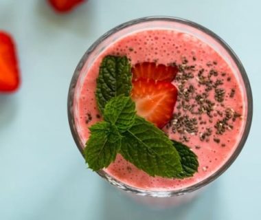 Vue en plongée sur un dessert glacé aux fruits rouges mixés, avec une fraise coupée et de la menthe en décoration