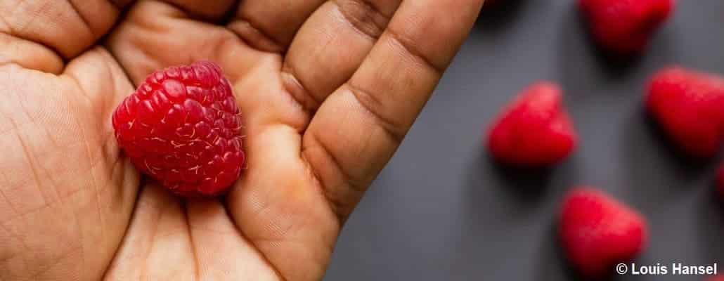 Framboise dans une main et quelques framboises en arrière plan