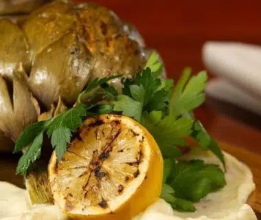 Un artichaut cuit avec un citron sur une planche en bois